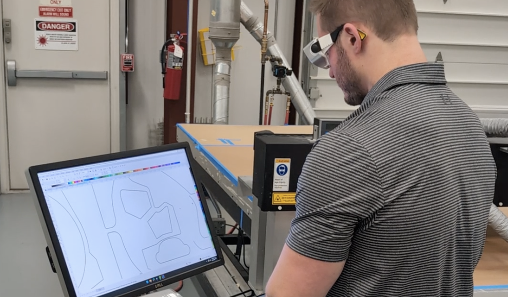 person wearing safety glasses standing in front of a computer monitor creating a light guide prototype